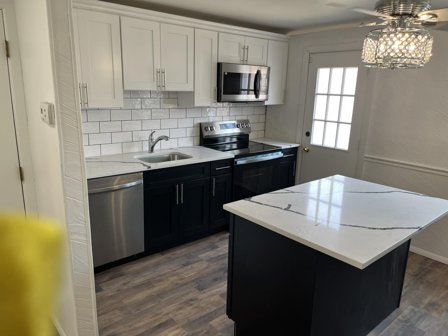 Renovated kitchen with white upper cabinets, dark lower cabinets, and island